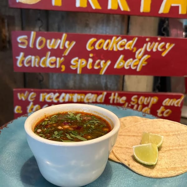 A La Lupe Cantina birria soup with tortillas and lime wedges on a blue plate.